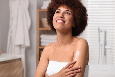 Photo of Beautiful young woman applying body cream onto arm in bathroom