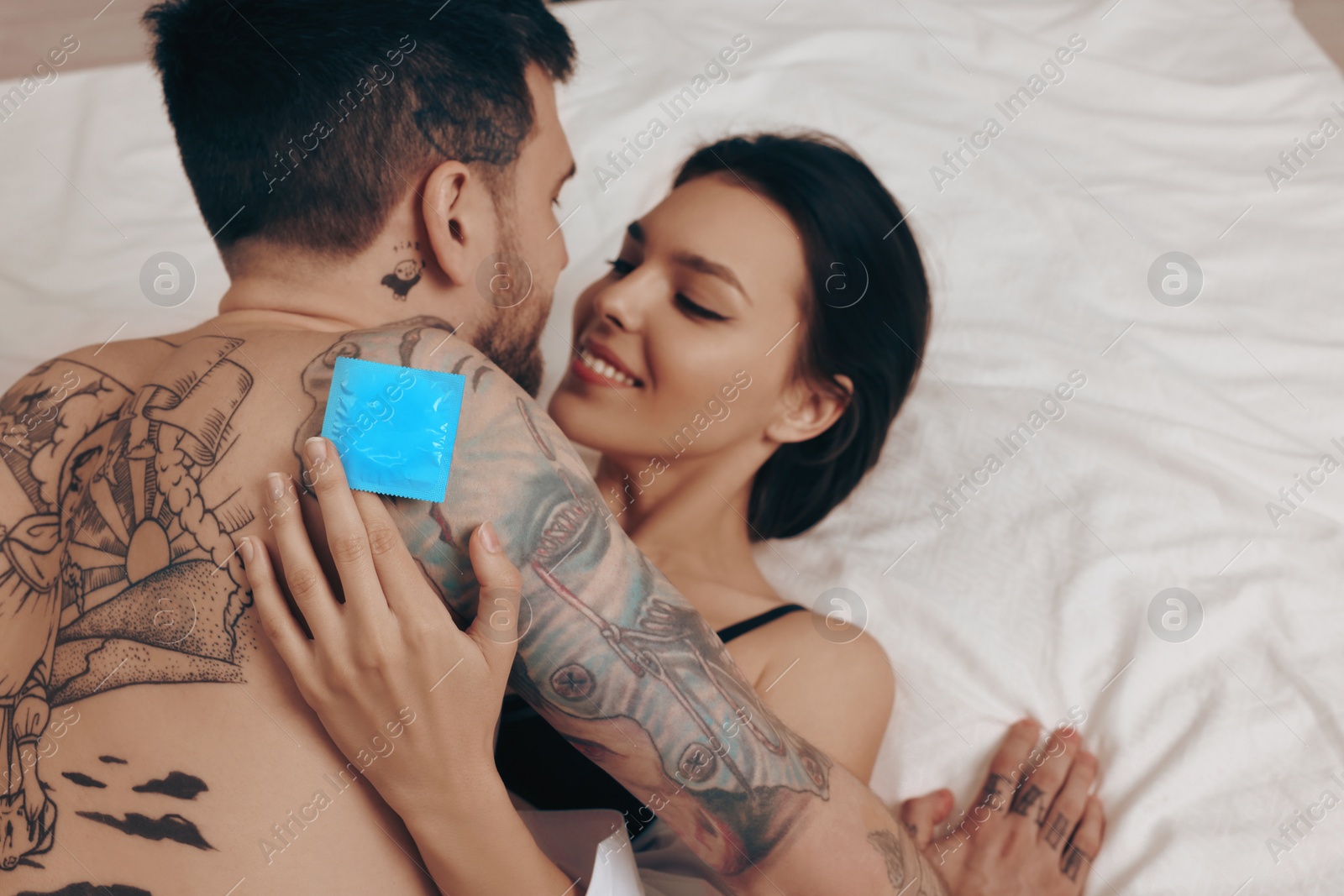 Photo of Couple having sex on bed. Woman holding condom