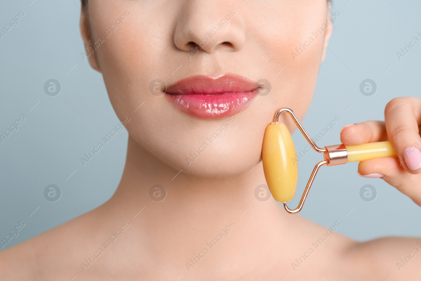 Photo of Woman using natural jade face roller on grey background, closeup