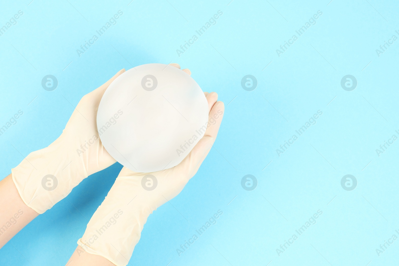 Photo of Doctor holding silicone implant for breast augmentation on color background, top view with space for text. Cosmetic surgery