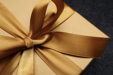 Photo of Golden gift box with satin bow on black background. closeup