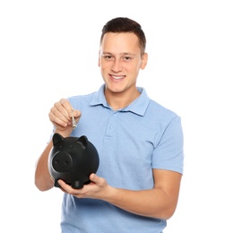 Young man putting money into piggy bank on white background