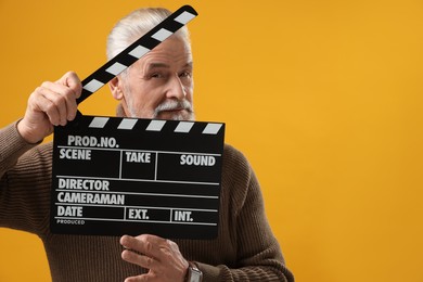 Photo of Senior actor holding clapperboard on yellow background, space for text. Film industry