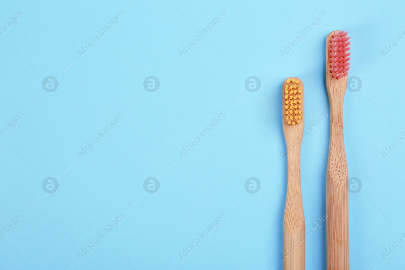 Photo of Toothbrushes made of bamboo on light blue background, flat lay. Space for text