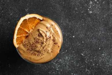 Photo of Glass of delicious dalgona coffee with dry orange and chocolate on grey textured table, top view. Space for text