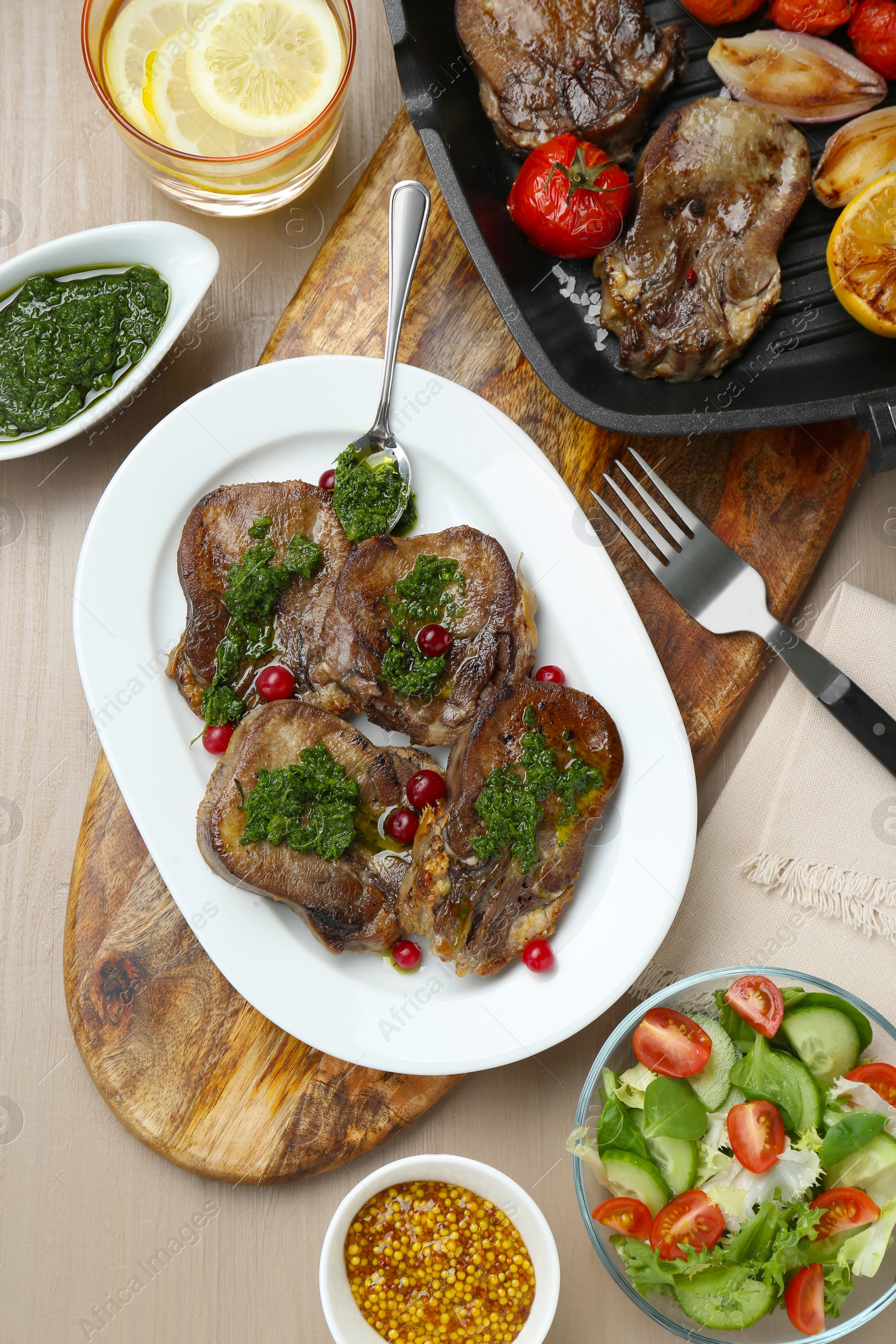 Photo of Tasty beef tongue pieces, salsa verde, berries, mustard and salad on beige wooden table, flat lay