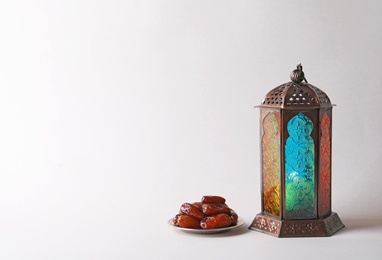 Photo of Muslim lamp with candle and dates on light background. Fanous as Ramadan symbol