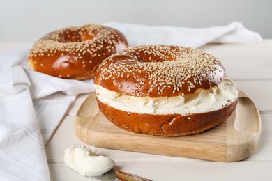 Photo of Delicious bagel with cream cheese on white wooden table