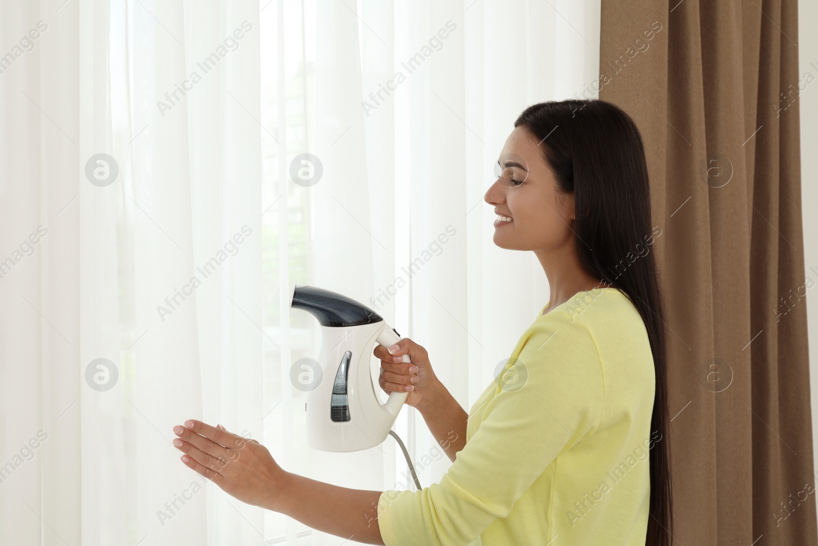 Photo of Woman steaming curtain near window at home. Space for text