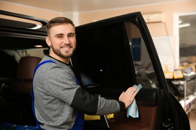 Smiling worker washing car window after tinting in shop