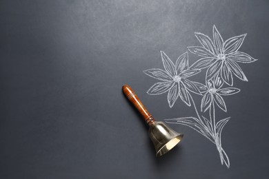 Photo of Golden bell and drawn flowers on black chalkboard, top view. School days