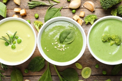 Photo of Flat lay composition with different fresh vegetable detox soups made of green peas, broccoli and spinach in dishes on wooden background