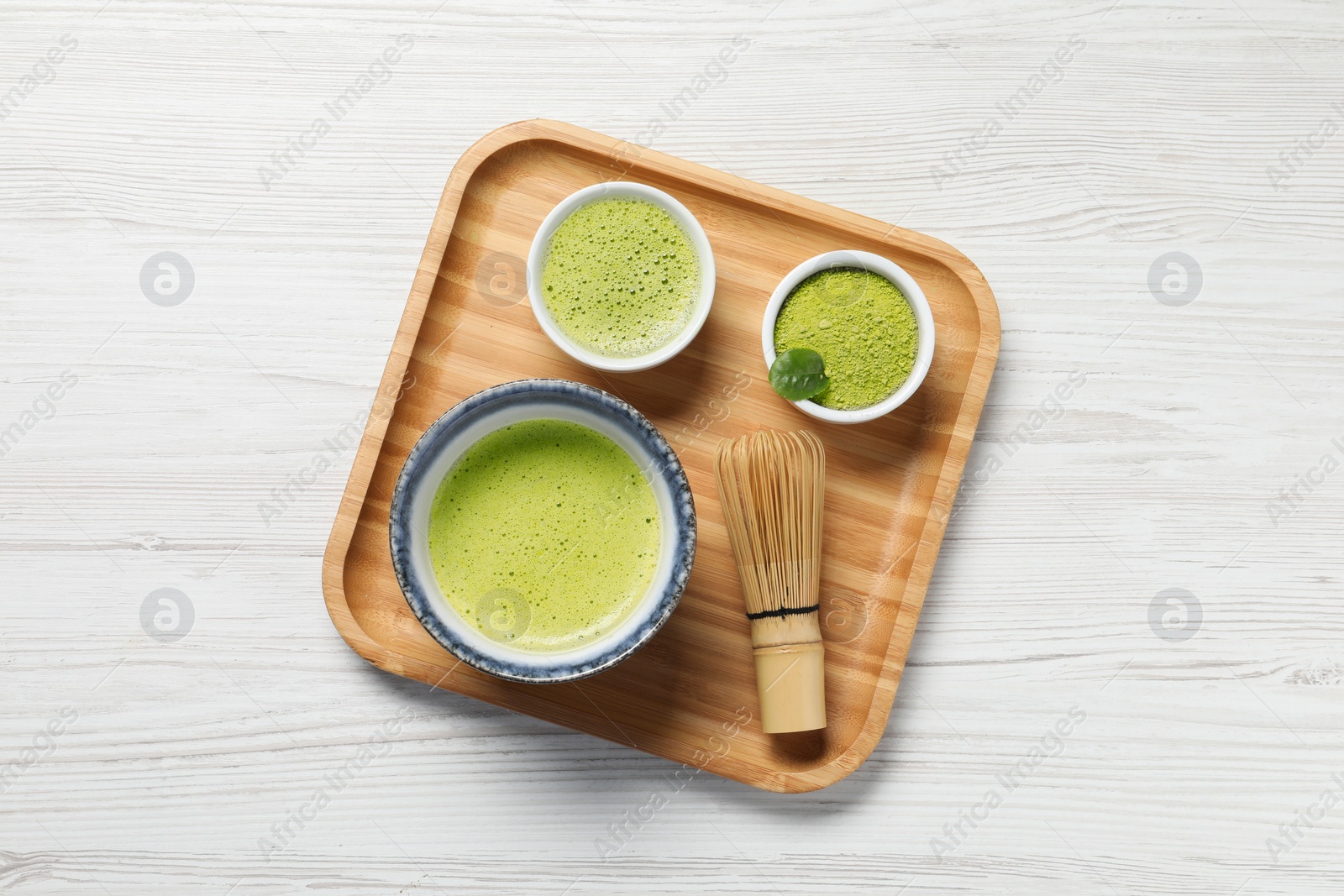 Photo of Fresh matcha tea, bamboo whisk and green powder on white wooden table, top view
