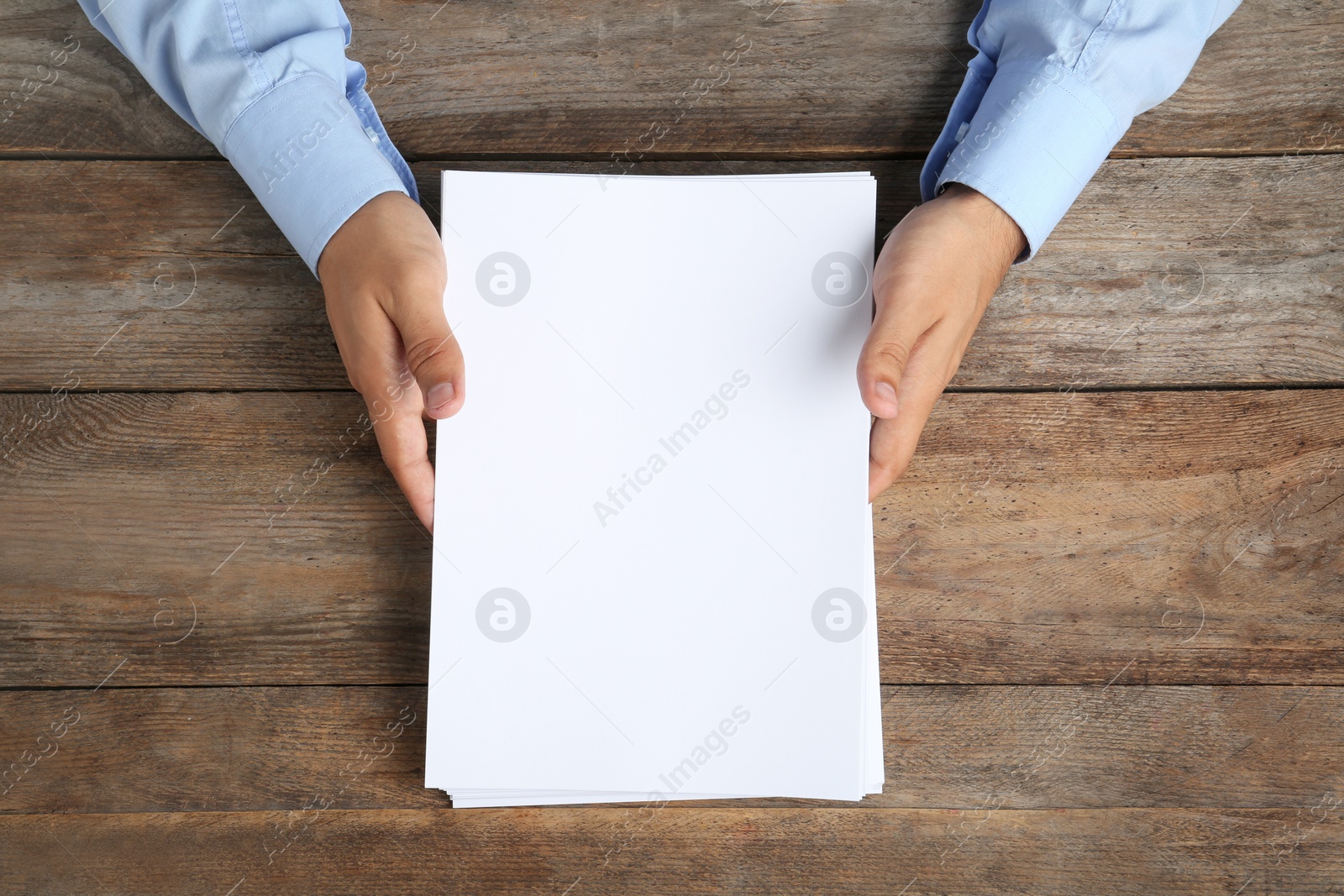 Photo of Man holding blank paper sheets for brochure at wooden table, top view. Mock up