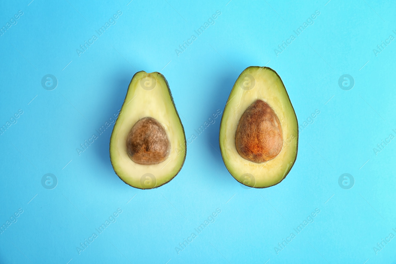 Photo of Halves of ripe avocados on color background, top view