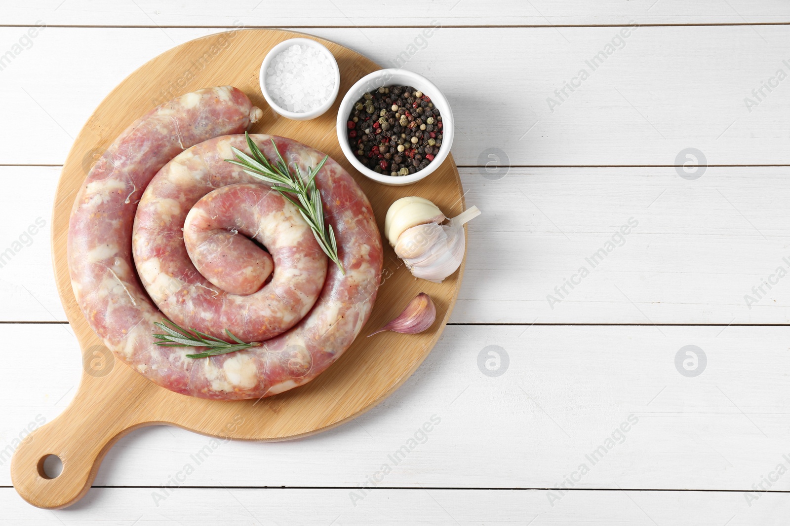 Photo of Raw homemade sausage, garlic and spices on white wooden table, top view. Space for text