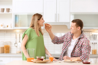 Happy lovely couple having breakfast with tasty toasted bread at table in kitchen