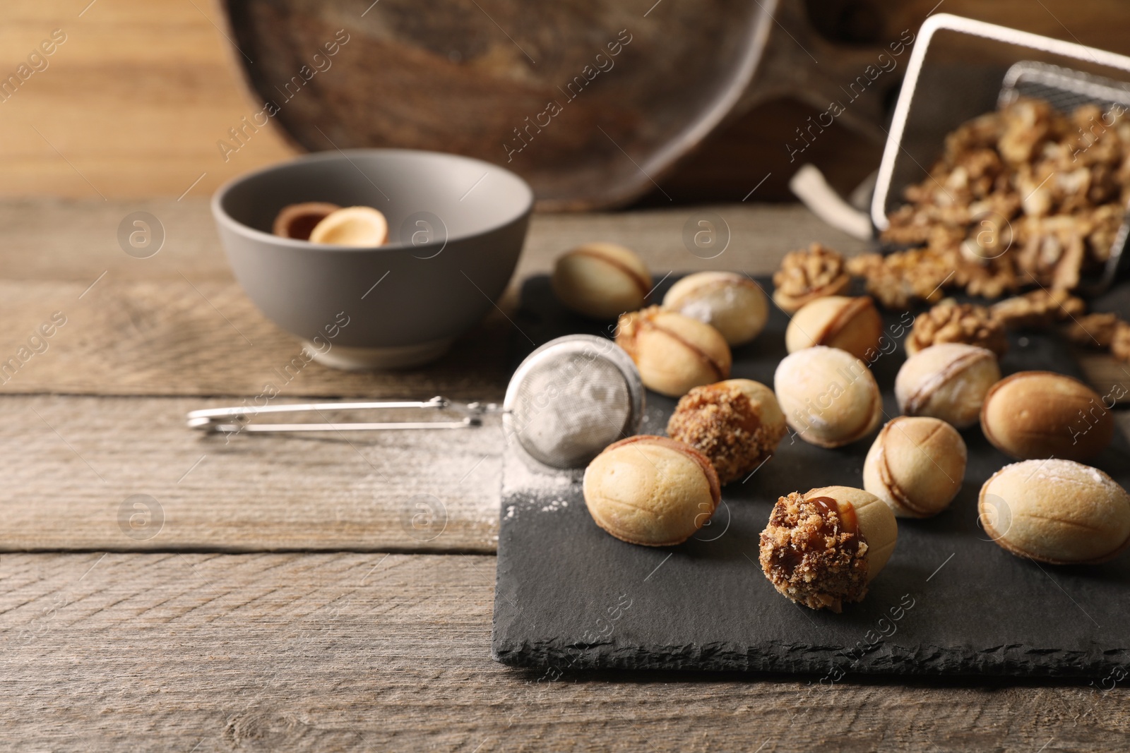 Photo of Freshly baked homemade walnut shaped cookies and flour on wooden table, space for text