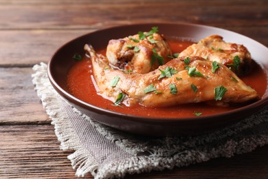 Photo of Tasty cooked rabbit meat with sauce and parsley on wooden table, closeup