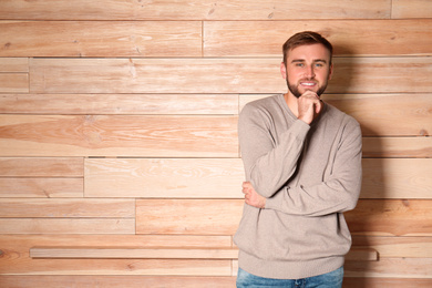 Handsome man wearing warm sweater on wooden background. Space for text