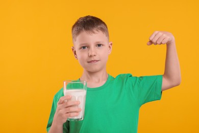 Photo of Cute boy with glassfresh milk showing his strength on orange background