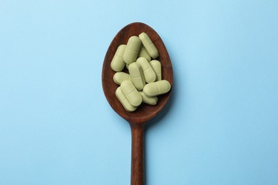 Photo of Vitamin pills in wooden spoon on light blue background, top view