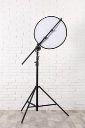 Professional light reflector on tripod near white brick wall in room. Photography equipment