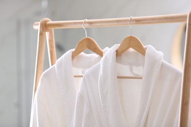 Fresh white bathrobes hanging on rack indoors