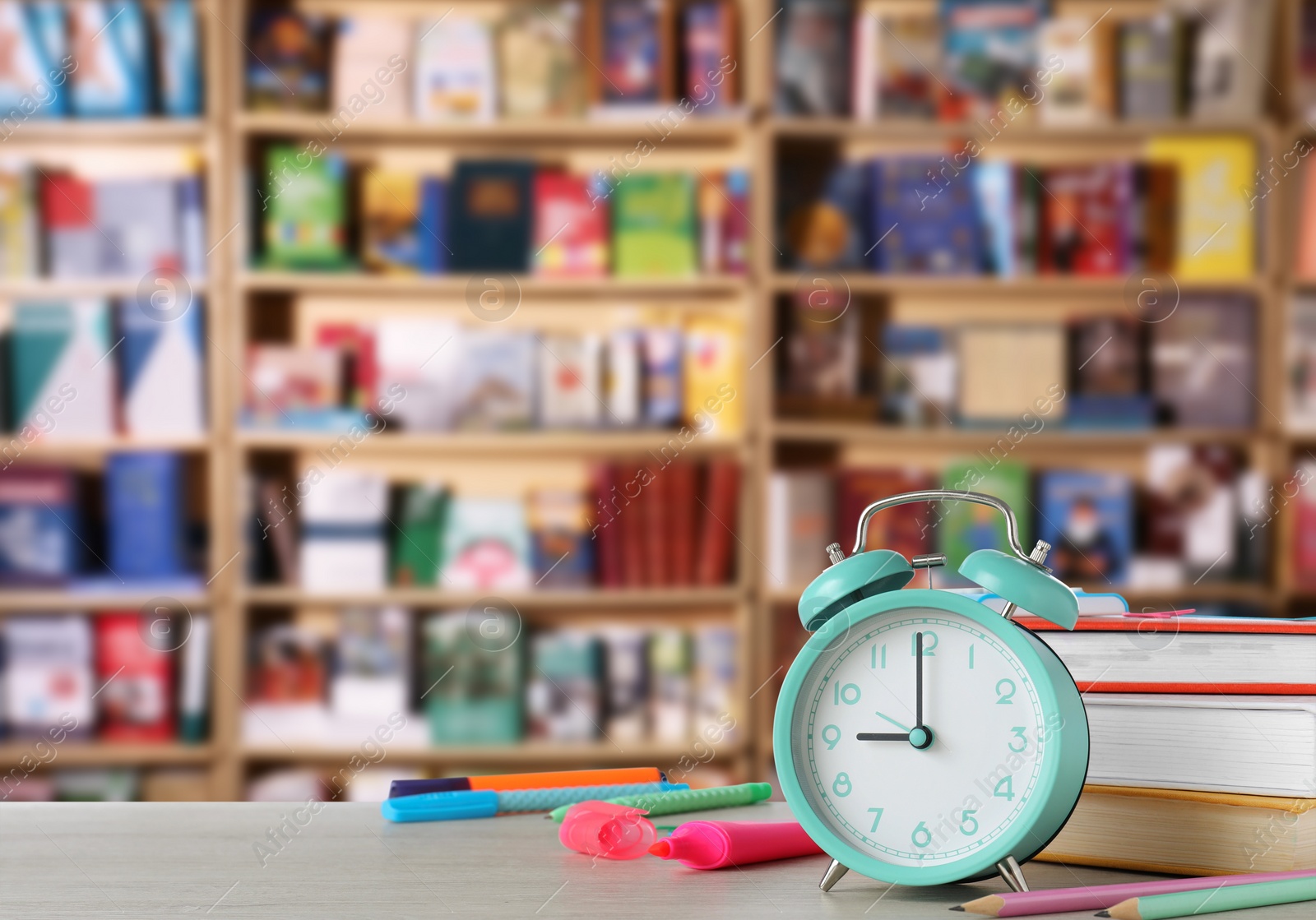 Image of Turquoise alarm clock and different stationery on wooden table in library, space for text