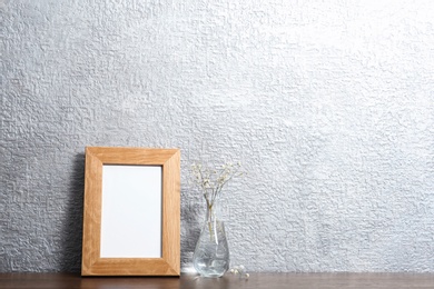 Photo of Blank frame and vase with flowers on table near color wall. Mock up for design