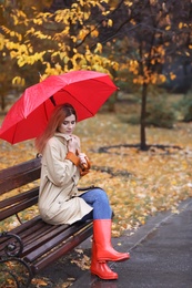 Photo of Woman with umbrella sitting on bench in autumn park. Rainy day