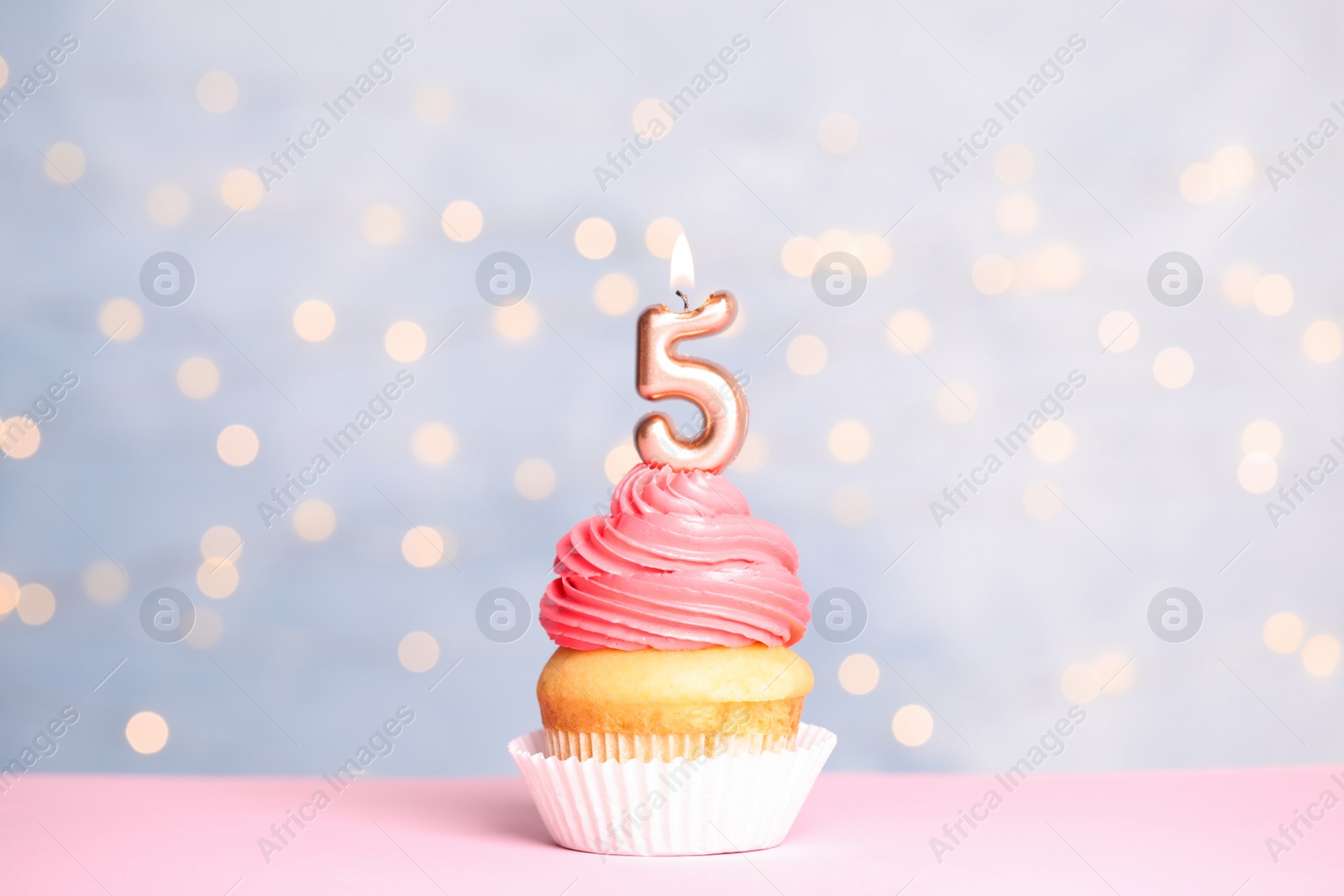 Photo of Birthday cupcake with number five candle on table against festive lights