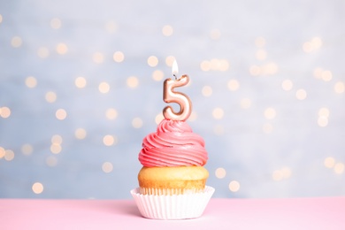 Photo of Birthday cupcake with number five candle on table against festive lights