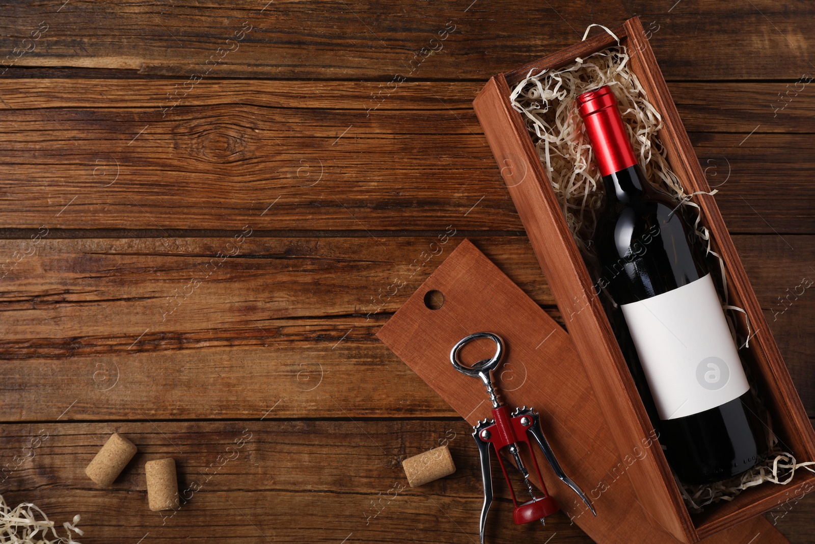 Photo of Box with wine bottle, corkscrew and corks on wooden table, flat lay. Space for text