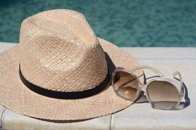 Photo of Stylish hat and sunglasses near outdoor swimming pool on sunny day, closeup. Beach accessories