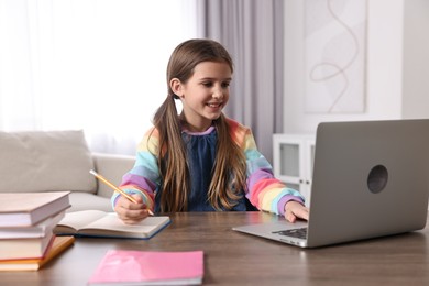 E-learning. Cute girl taking notes during online lesson at table indoors