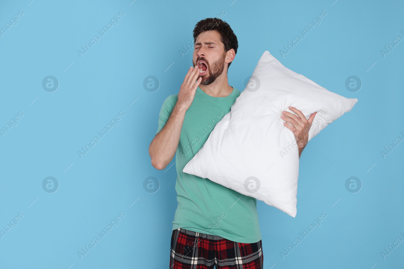 Photo of Tired man with pillow yawns on light blue background, space for text