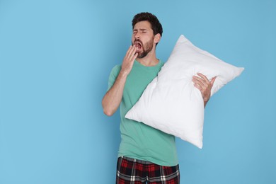 Photo of Tired man with pillow yawns on light blue background, space for text