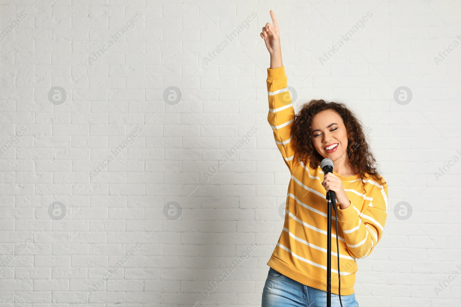 Photo of Portrait of curly African-American woman singing in microphone near brick wall. Space for text