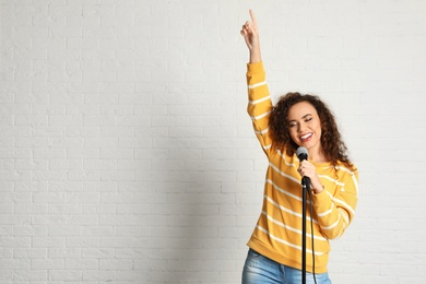 Photo of Portrait of curly African-American woman singing in microphone near brick wall. Space for text