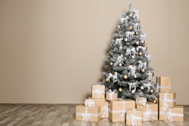 Photo of Decorated Christmas tree and gift boxes near beige wall. Space for text