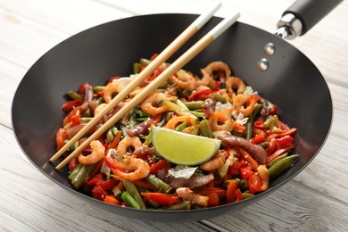 Shrimp stir fry with vegetables in wok and chopsticks on light wooden table