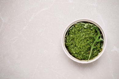 Bowl of tasty arugula pesto on light table, top view. Space for text