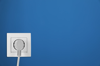 Image of Blue wall with power socket and inserted plug, space for text. Electrical supply