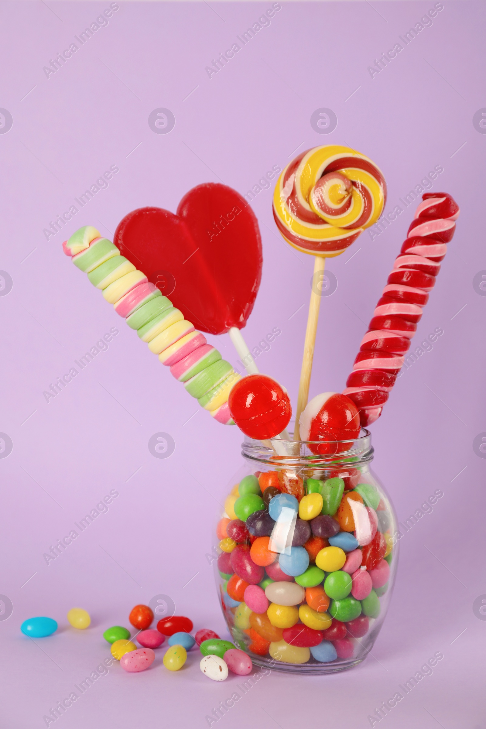 Photo of Glass jar with different candies on pale violet background