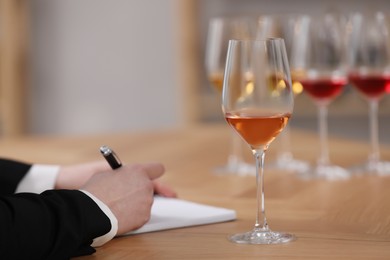 Photo of Sommelier making notes during wine tasting at table indoors, closeup