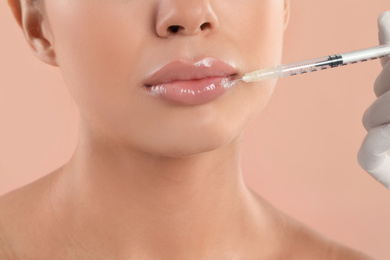 Photo of Young woman getting lips injection on peach background, closeup