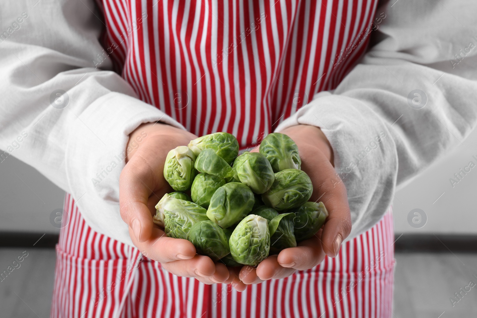 Photo of Woman holding pile of fresh green brussels sprouts, closeup