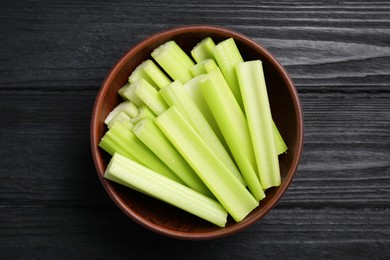 Photo of One bowl of fresh cut celery on black wooden table, top view