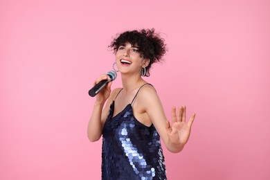 Beautiful young woman with microphone singing on pink background